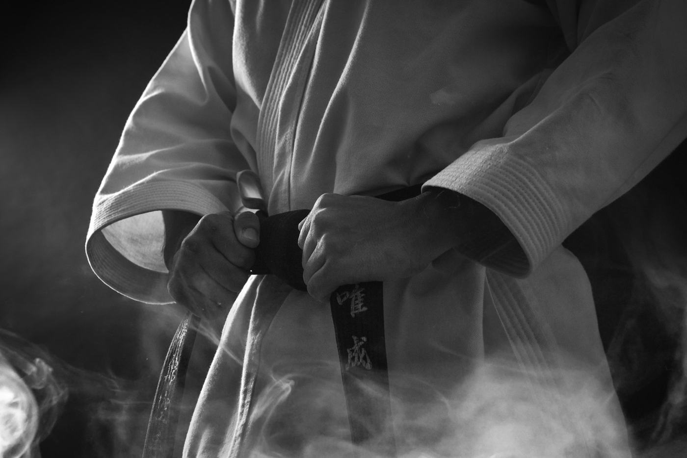 A martial artist tying the belt of a white gi